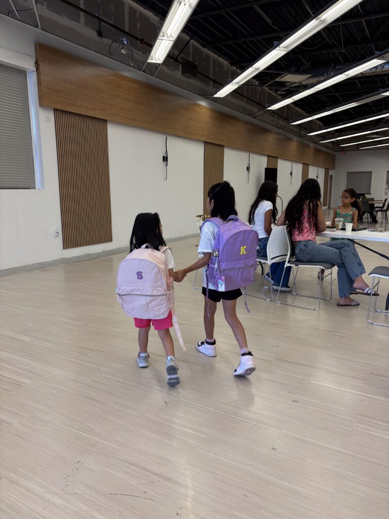 Two kids walking joyfully with their new backpacks after a giveaway event.
