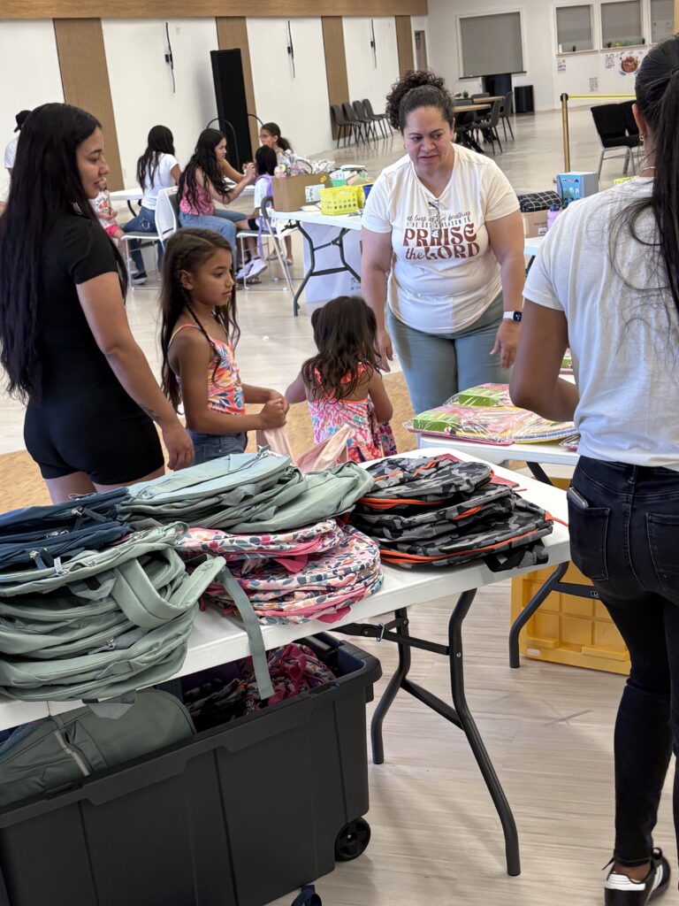 Two children and three adults talking and looking at backpacks during a backpack giveaway event in Boise, Idaho.
